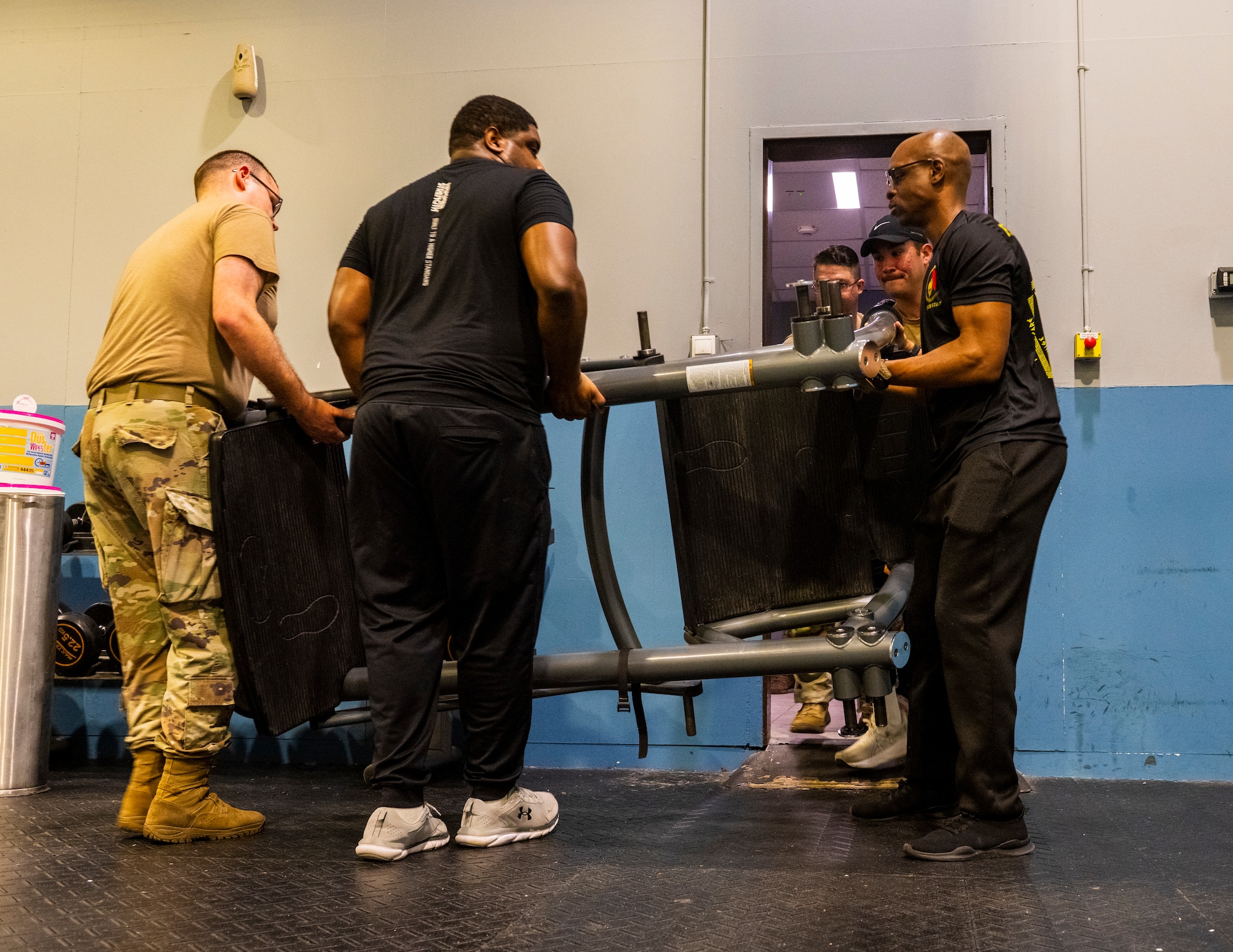 U.S. Airmen maneuver a strength-training machine through a doorway