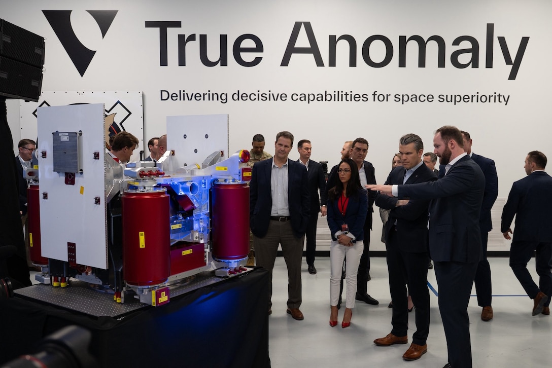 Secretary Pete Hegseth talks to civilians in a room with "True Anomaly" on the wall.