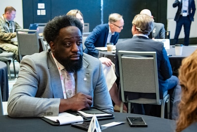 A man wearing a light gray suit sits at a table.