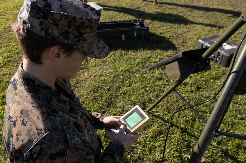 A woman in a camouflage military uniform works on a piece of military weather equipment.