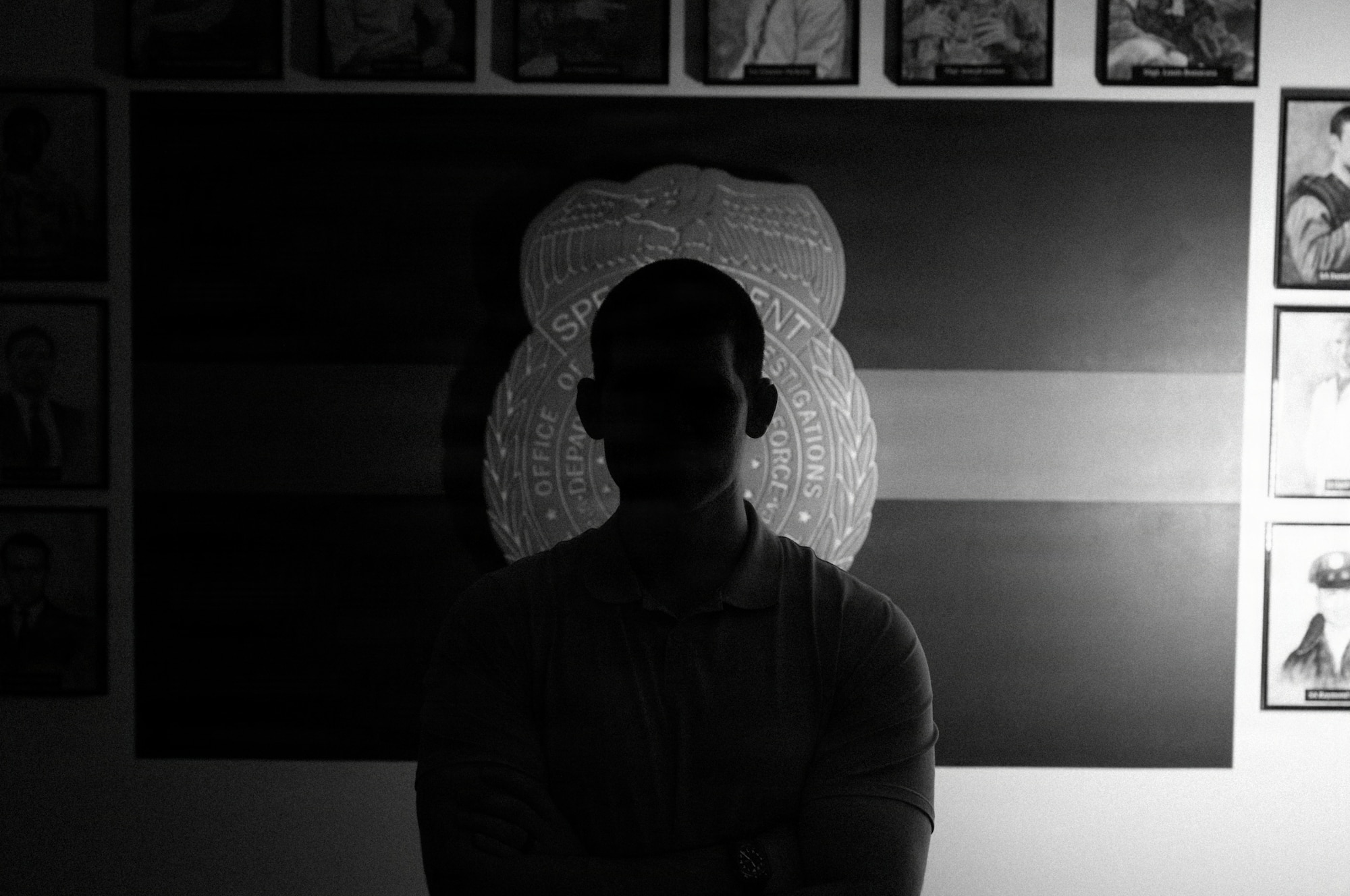 A U.S. Air Force Office of Special Investigations special agent stands near an AFOSI emblem and photos honoring fallen agents during a staged photo at Seymour Johnson Air Force Base, North Carolina, Feb. 11, 2026. AFOSI special agents serve worldwide to protect the Air Force and seek the truth in support of national defense. (U.S. Air Force photo by Airman 1st Class Holly Leonard)