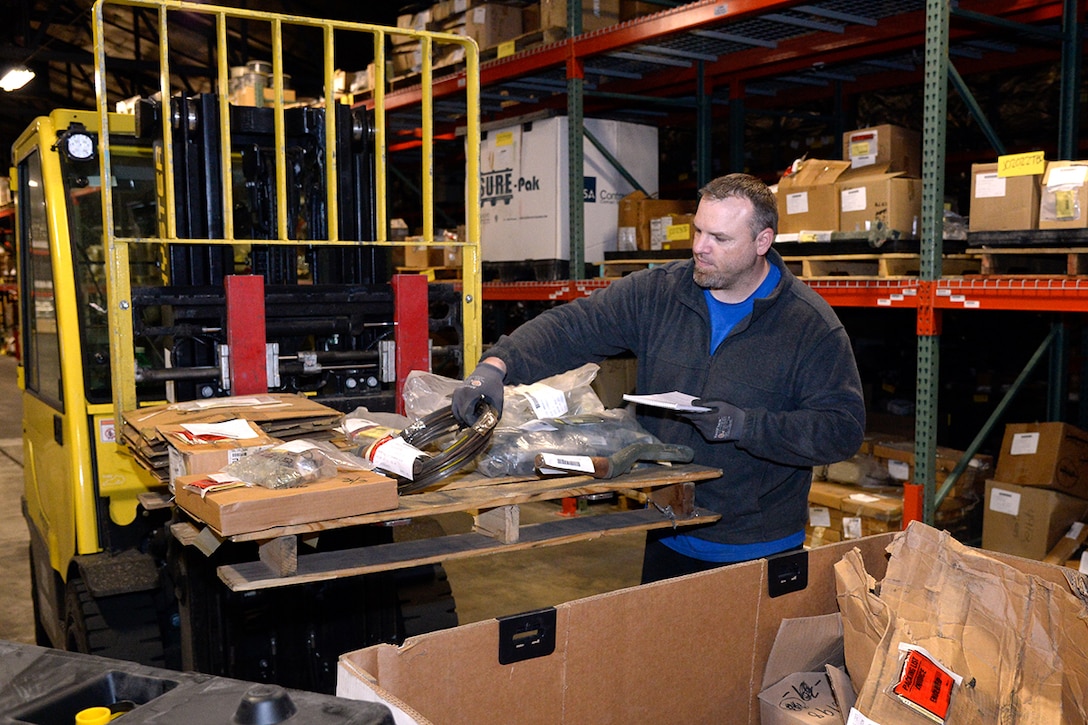 A man in a warehouse picks up small items in bags to process them.