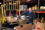 A man in a warehouse picks up small items in bags to process them.