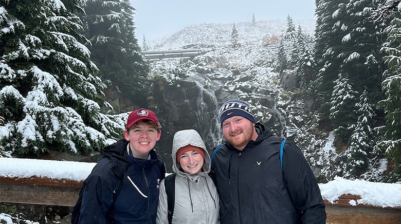 Three people standing in front of a snowy scenery.