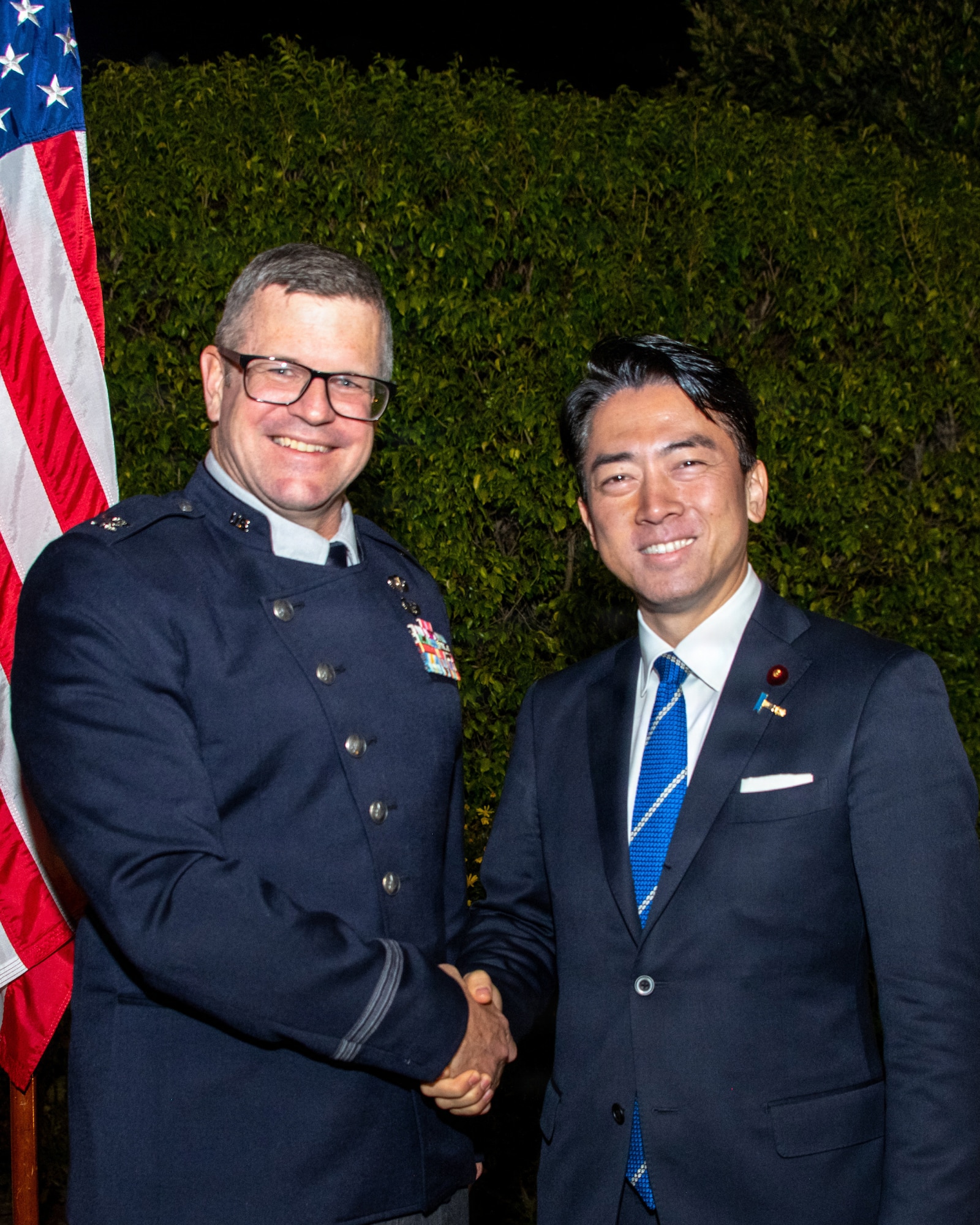 Two gentlemen, one in a U.S. Space Force formal uniform, pose and smile for the camera as they shake hands.
