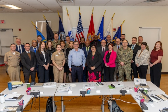 Large group posing for photo with flags behind and tables in front.