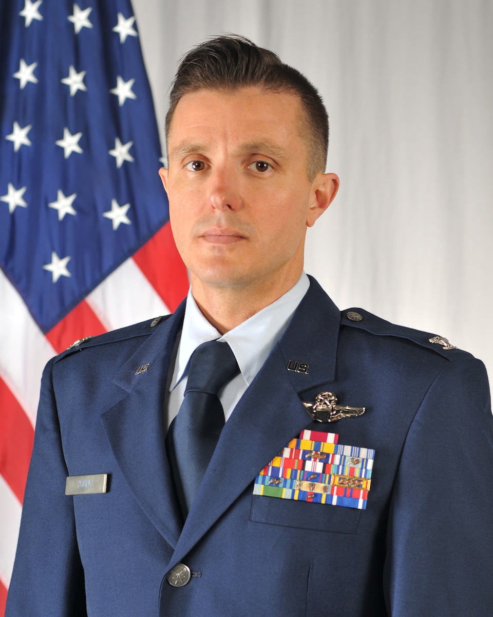Pictured is Colonel Benjaman Young in Class A dress uniform while standing in front of the flag of the United States.