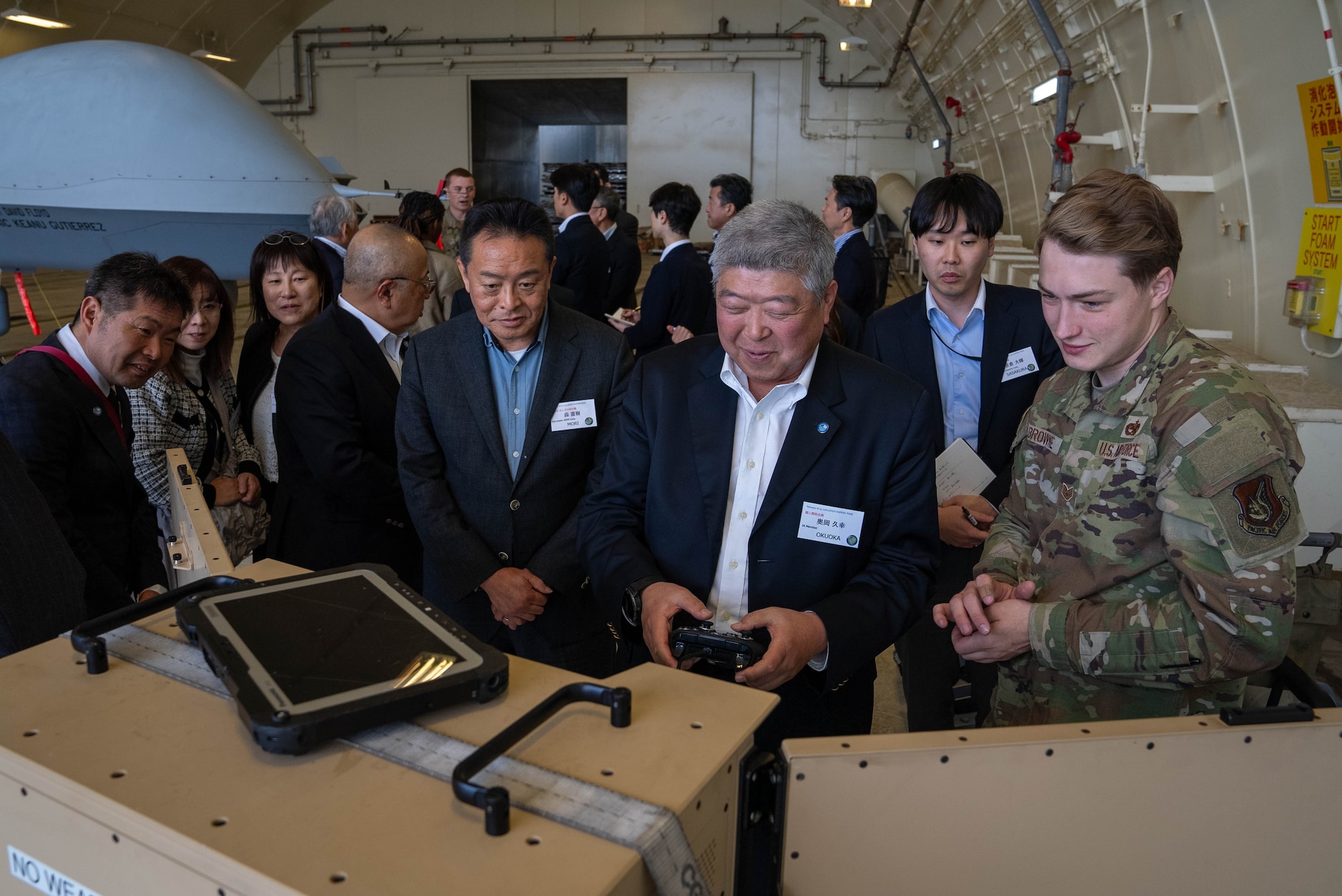 U.S. Air Force Staff Sgt. Edgar Browne, 319th Expeditionary Reconnaissance Squadron avionics noncommissioned officer in charge, assists members of the Japan-America Air Force Goodwill Association with an interactive display demonstrating MQ-9 Reaper capabilities during a tour at Kadena Air Base, Feb. 18, 2026.