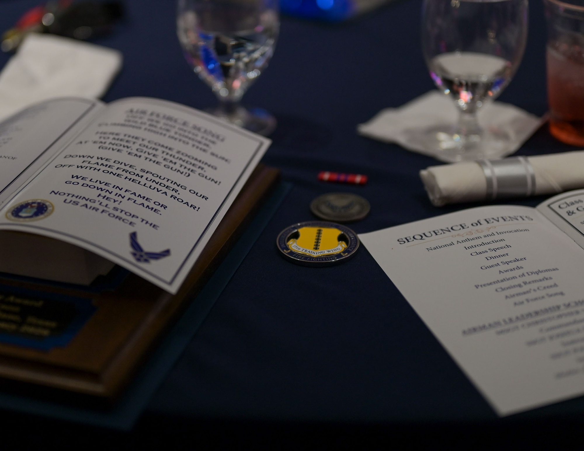 Two open programs sit on a black tablecloth while a challenge coin, an airman's coin and service dress ribbon are centered between them.