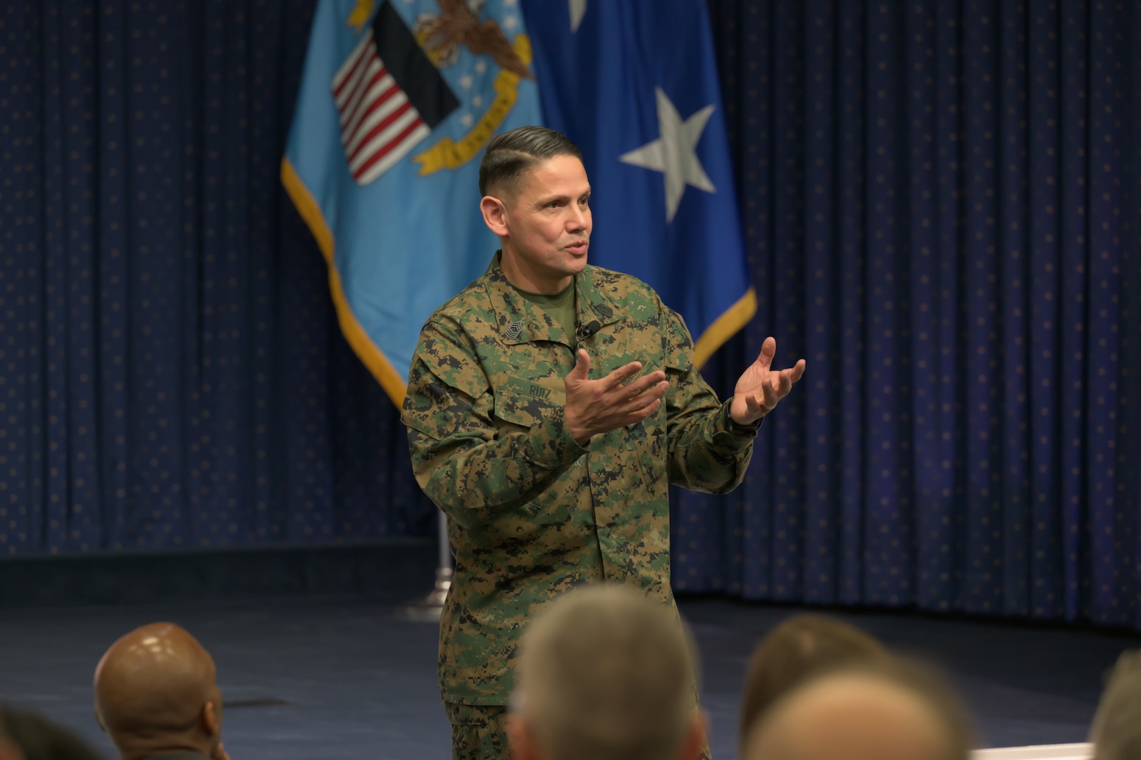 The sergeant major of the U.S. Marine Corps dressed in a uniform stands on a stage.