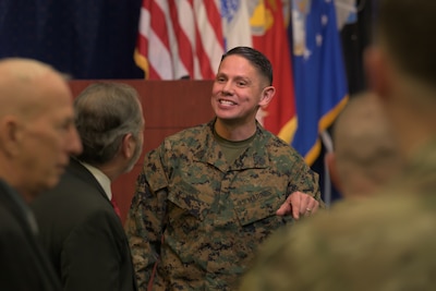 A Marine in uniform stands among people in civilian clothes.