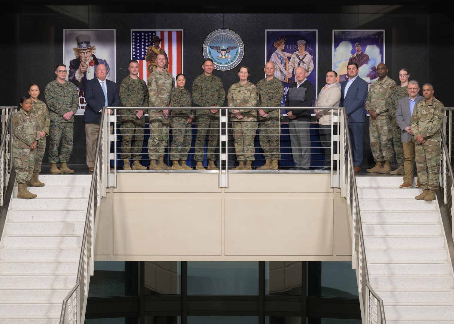 A group of service members in uniform and several civilians in plain clothes pose on a stairwell.