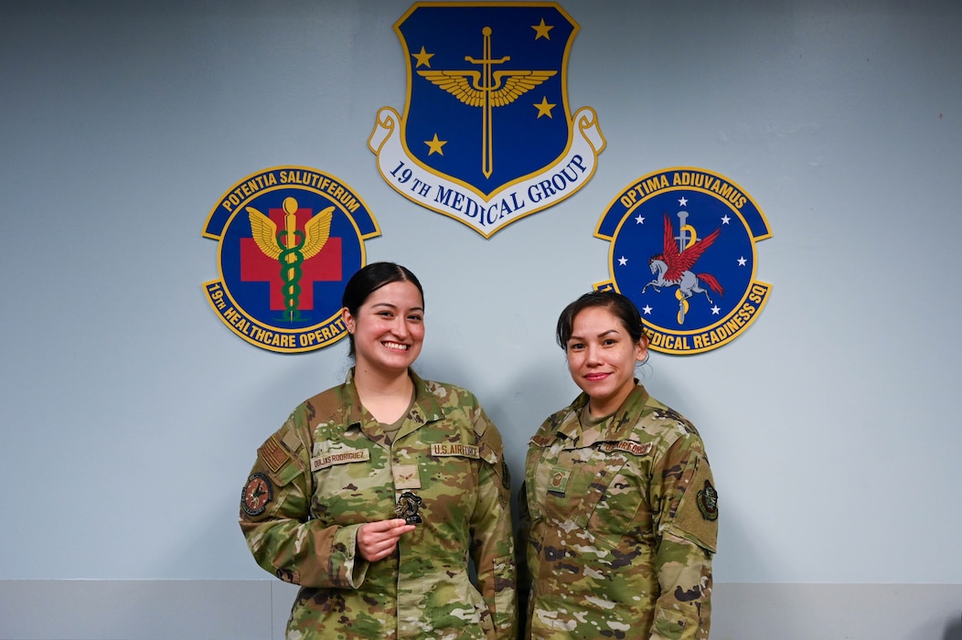 Two women pose in front of a logo.