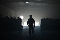 photo silhouette of an air force Airmen inside a dark warehouse with some light creeping behind him