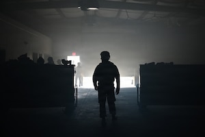 photo silhouette of an air force Airmen inside a dark warehouse with some light creeping behind him