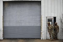 photo of two air force Airmen in protective helmet and vest exiting a warehouse through a door