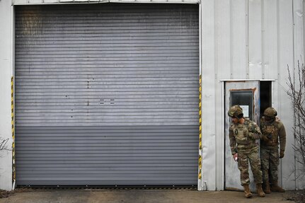 photo of two air force Airmen in protective helmet and vest exiting a warehouse through a door