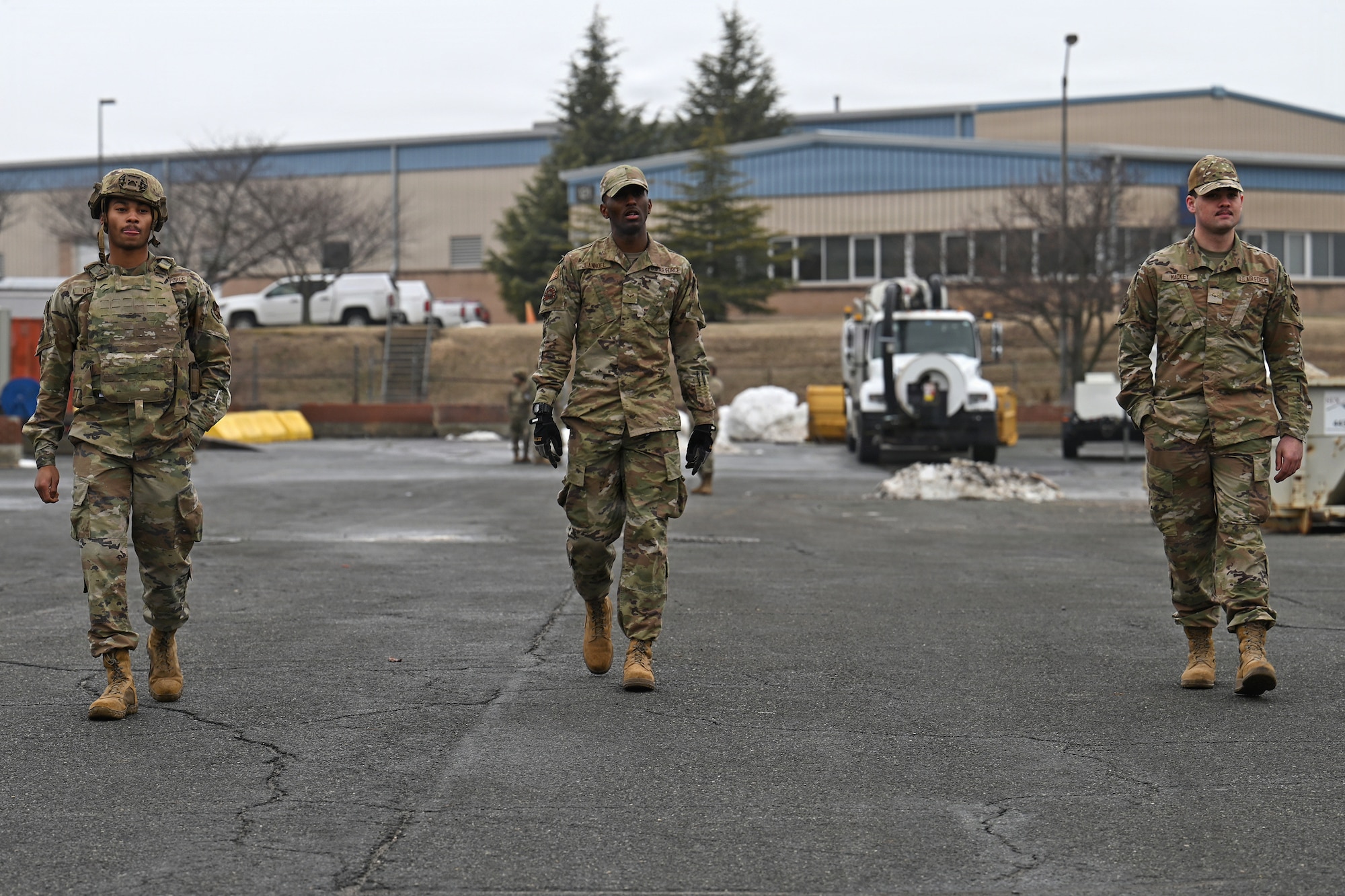 Photo of three Airmen in protective gear walking down a compound searching for simulated unexploded ordnance
