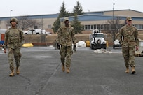 Photo of three Airmen in protective gear walking down a compound searching for simulated unexploded ordnance