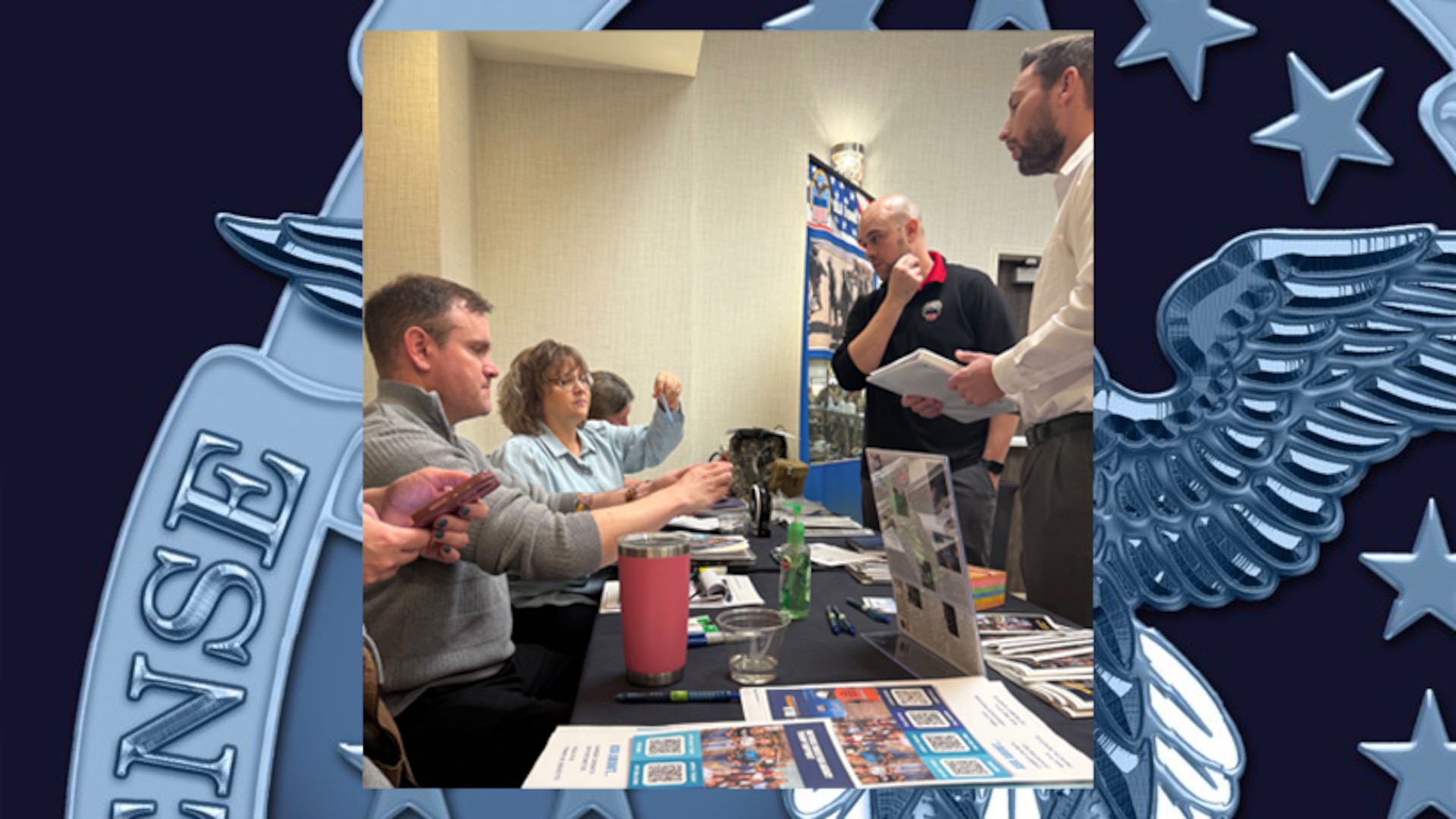 Photo shows group of people attending a job fair, some sitting, some standing.