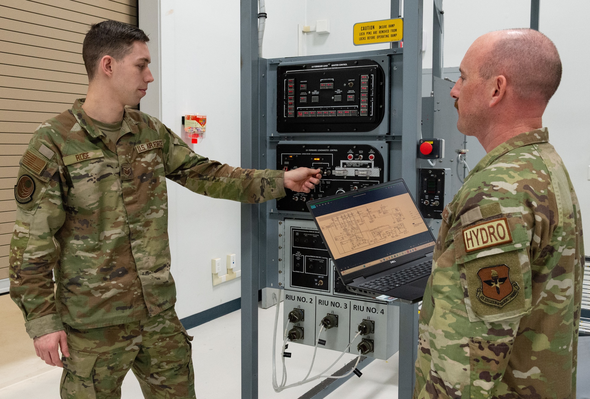 U.S. Air Force Master Sgt. Justin Goode, right, Air Force Career Development Academy learning engineer, watches Staff Sgt. Weston Rose, left, 373rd Training Squadron, Detachment 3 C-5M hydraulic instructor, operate the C-5 forward ramp maintenance training device located at the 373rd TRS, Det 3 on Dover Air Force Base, Delaware, Feb. 12, 2026. Goode observed the opening and closing operation of the forward ramp to identify what imagery may be needed to develop Computer-Based Training micro-lessons for hydraulic system maintenance personnel. (U.S. Air Force photo by Roland Balik)