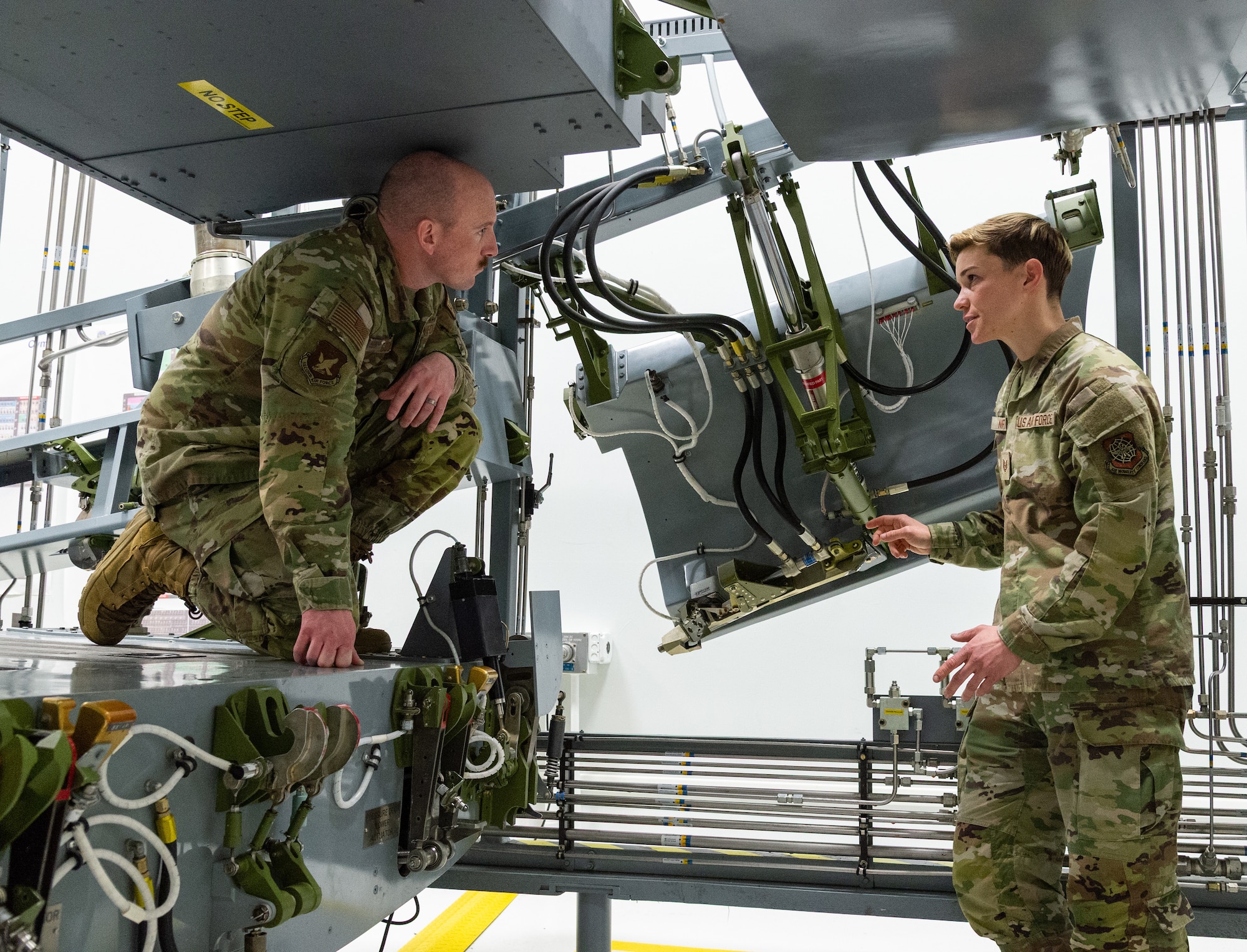 U.S. Air Force Master Sgt. Justin Goode, left, Air Force Career Development Academy learning engineer, listens to Tech. Sgt. Ashleigh Norris, right, 436th Maintenance Group Maintenance Qualification Training Program hydraulics instructor, describe components on the C-5 aft ramp side door maintenance training device located at the 373rd TRS, Det 3 on Dover Air Force Base, Delaware, Feb. 12, 2026. Norris pointed out key hydraulic components and side door operation to gain knowledge on how the system works. (U.S. Air Force photo by Roland Balik)
