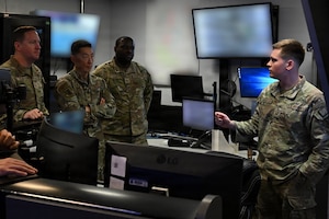 U.S. Air Force Staff Sgt. Joel A. Ezzi, 316th Security Forces Squadron Base Defense Operations Center controller, explains his duties to Col. Jun S. Oh, 316th Wing and installation commander, and Chief Master Sgt. Kevin W. Helms, 316th Wing command chief, during the February “Winnin’ Like a Griffin” recognition at Joint Base Andrews, Maryland, Feb. 17, 2026. Ezzi was recognized for leading training and readiness programs within his flight and serving as the squadron’s lead BDOC controller during the wing combat readiness inspection and the installation’s largest airshow in decades.