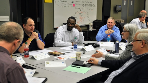 Students sit around a table discussing and collaborating with papers and notes in front of them.