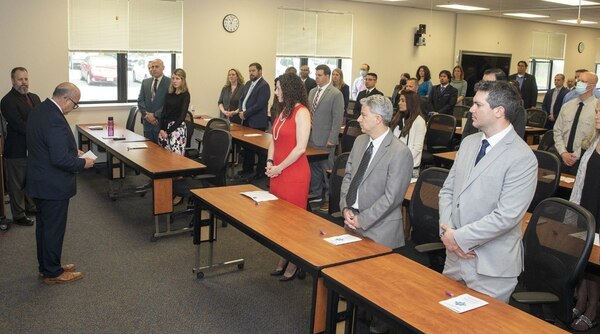 Students stand in a classroom while a professor delivers a speech at the front of the room.