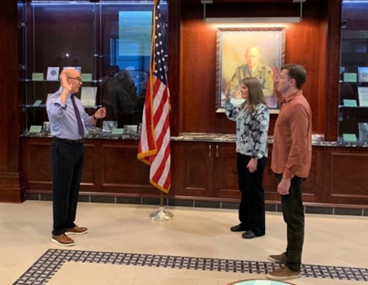 Man administering an oath to two civilians, a man and a woman, during a formal ceremony.