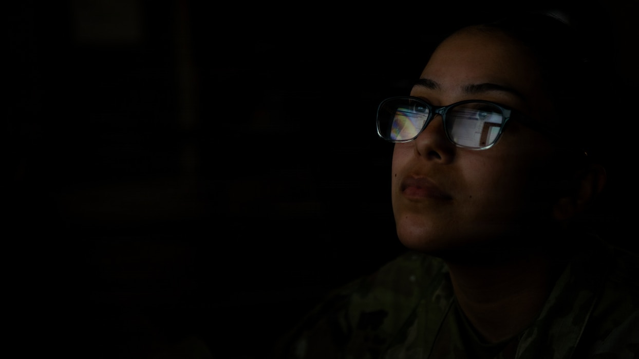 Airman viewing computer screen in the dark.