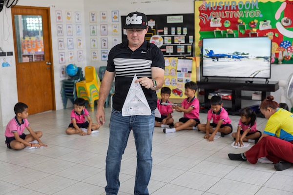 U.S. Navy Reserve Lt. Cmdr. Joe Morris, Military Sealift Command Navy Reserve Expeditionary Port Unit Little Rock, Ark., MSC Far East, demonstrates building a paper airplane to kids of the Learning Center, Human Help Network, during a community relations event at Pattaya, Thailand, Feb. 16, 2026.