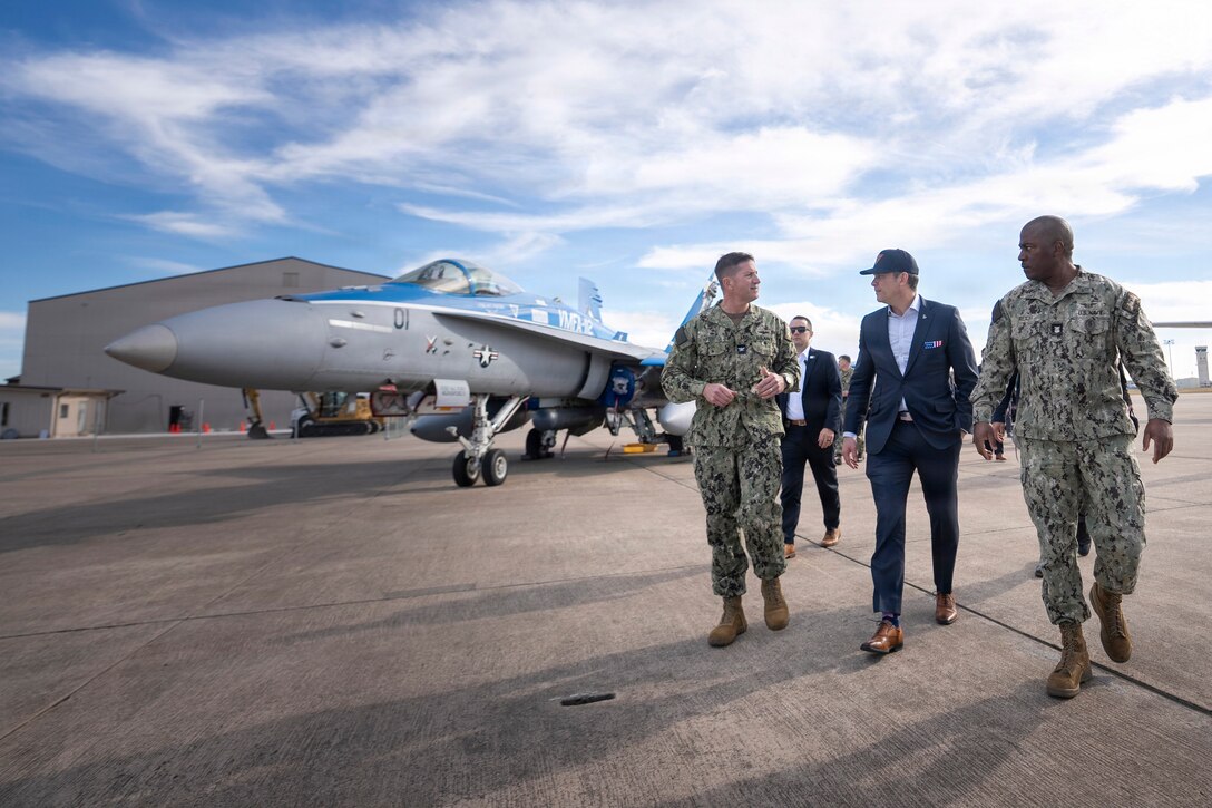Secretary of War Pete Hegseth walks with service members near a jet parked on a flight line.