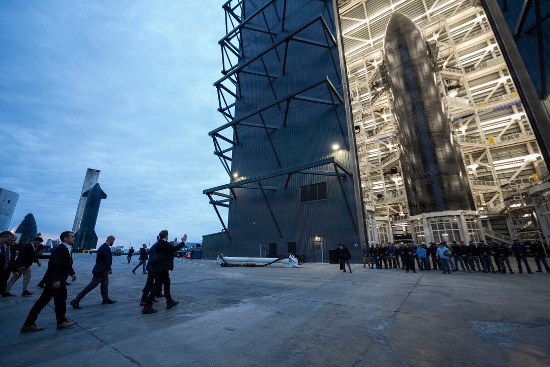 People walk outdoors toward a large building featuring a rocket nose-type display.