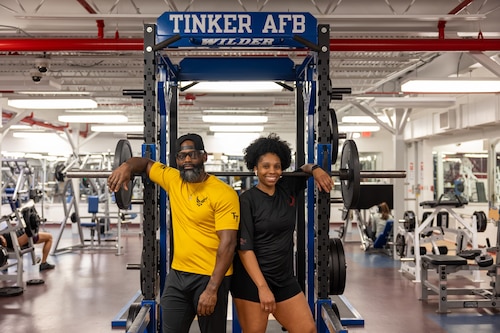 Man and woman stand in front of gym equipment.