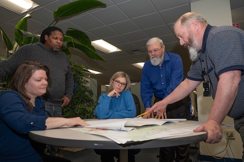 Five people standing around a table with papers on it.