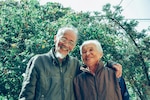 Elderly man and woman smile together in front of greenery