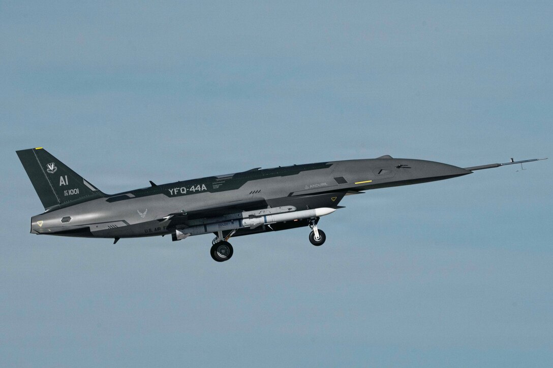 An aircraft flies with its wheels out and a blue sky in the background.