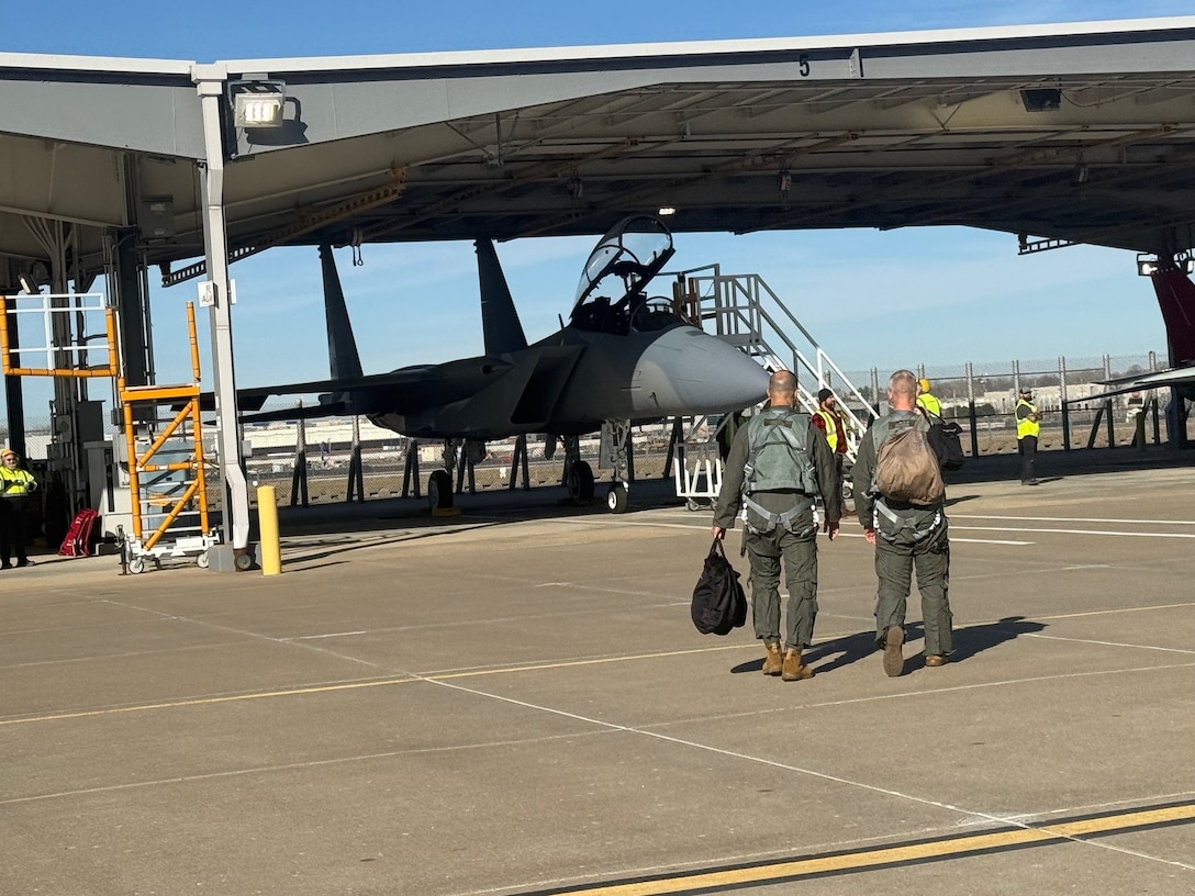 Two men in flight suits walk toward a plane