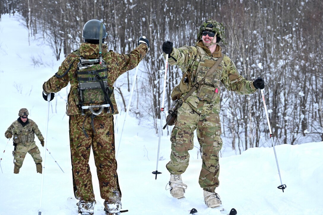 A U.S. and a Japanese soldier on skis in snow hold their fists up to bump.