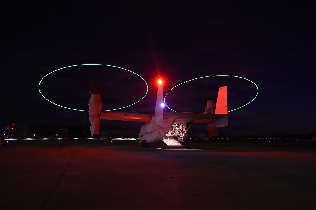 A military aircraft prepares to take off from a tarmac at night. The aircraft's rear cargo door is open.