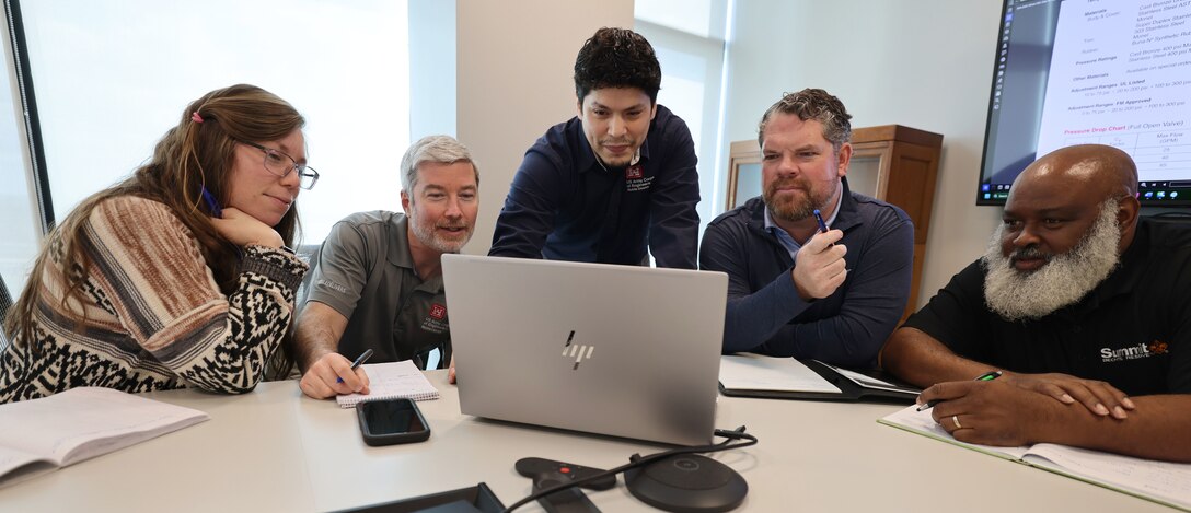 5 people siting looking at a laptop screen.