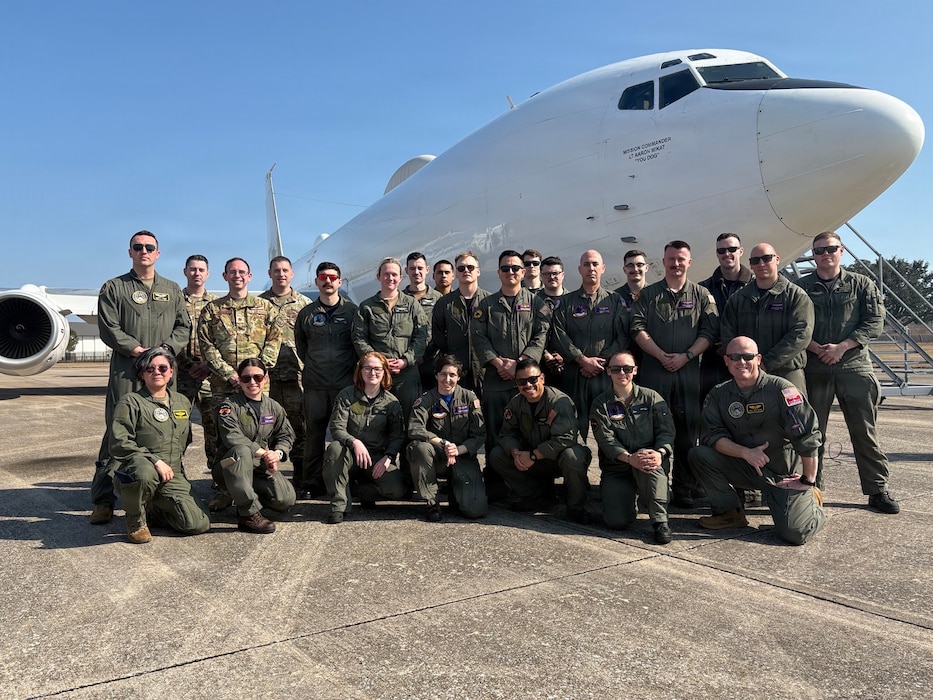 A group of service members pose in front of a white plane.