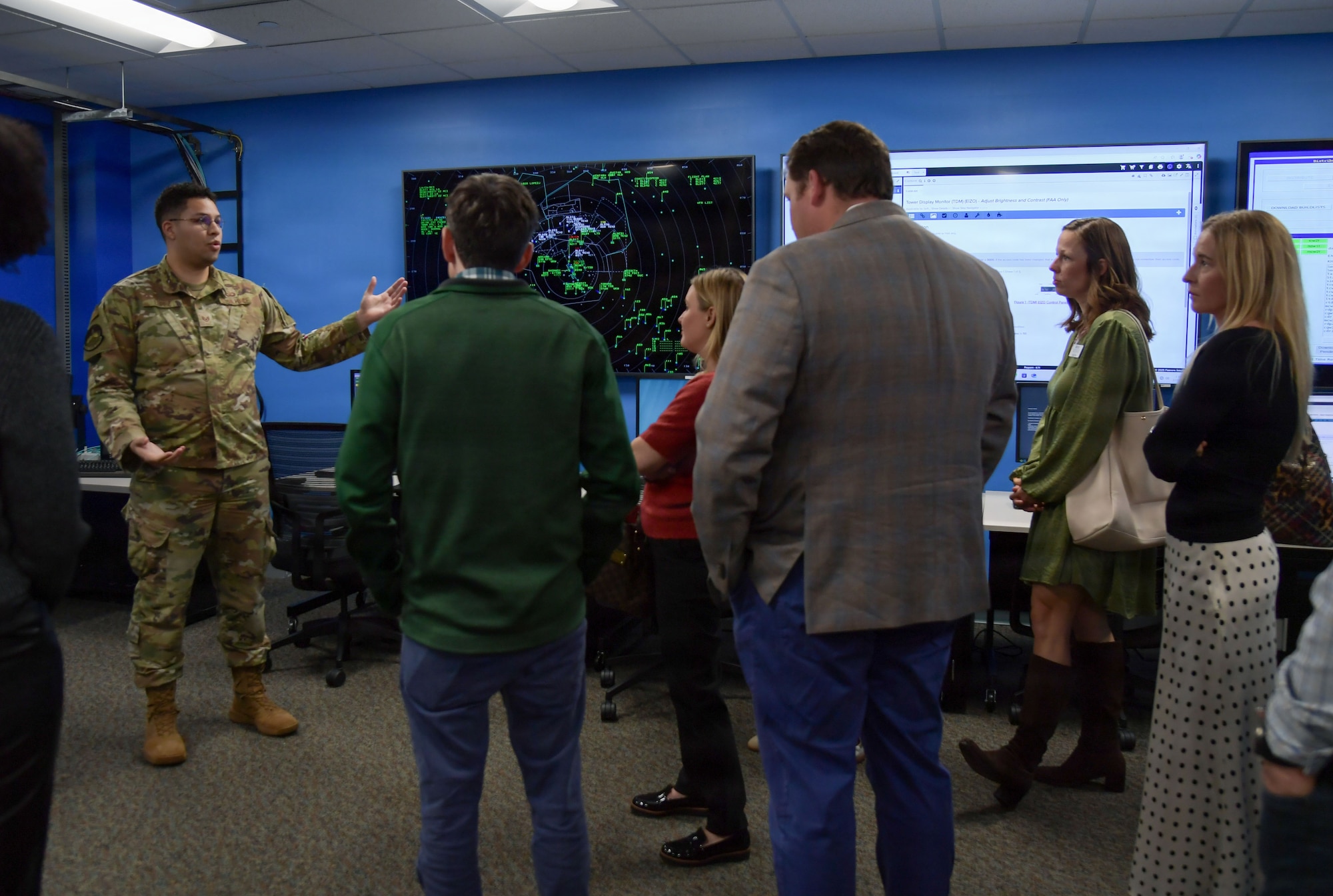 A man in Air Force uniform speaks to a group of people in front of a radar monitor.