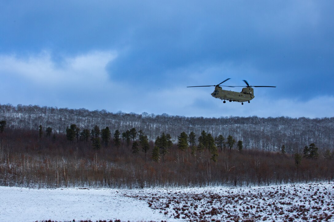 A man wearing a camouflage military uniform prepares for a parachute jump outside in a snow covered field.