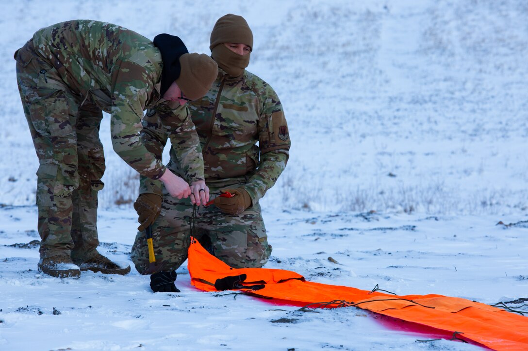 A man wearing a camouflage military uniform prepares for a parachute jump outside in a snow covered field.