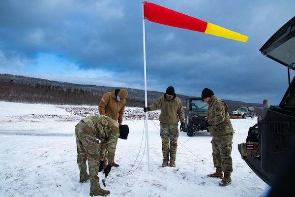 A man wearing a camouflage military uniform prepares for a parachute jump outside in a snow covered field.