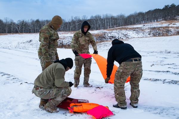 A man wearing a camouflage military uniform prepares for a parachute jump outside in a snow covered field.
