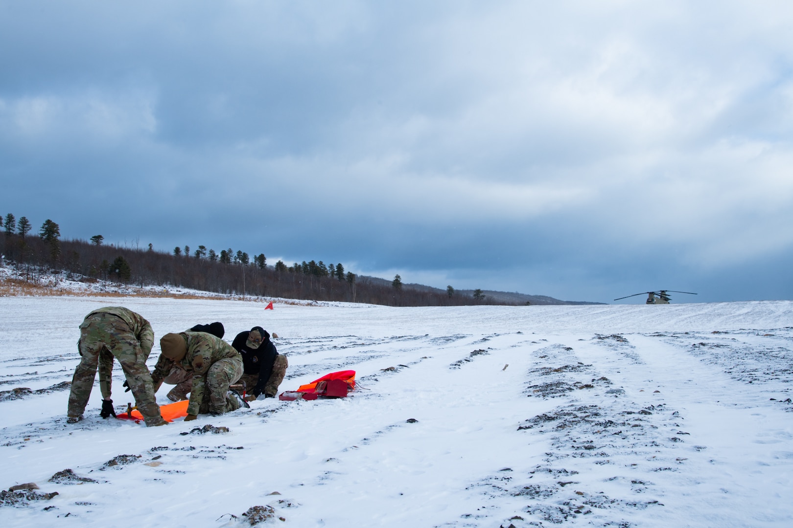 A man wearing a camouflage military uniform prepares for a parachute jump outside in a snow covered field.