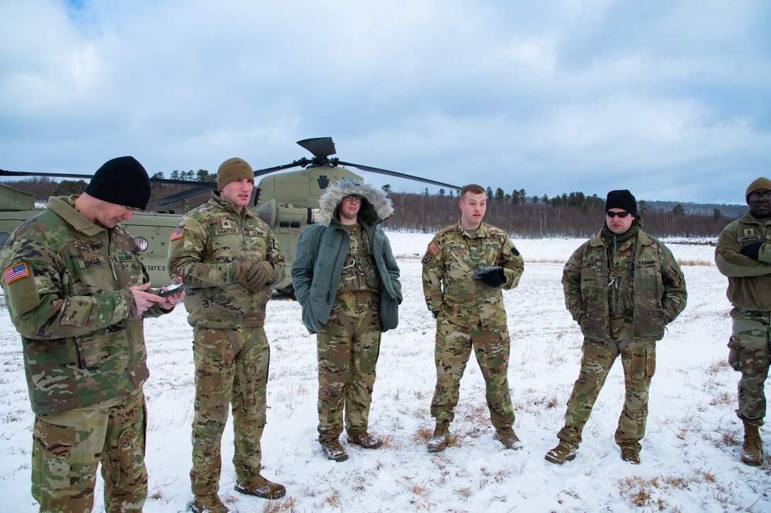A man wearing a camouflage military uniform prepares for a parachute jump outside in a snow covered field.